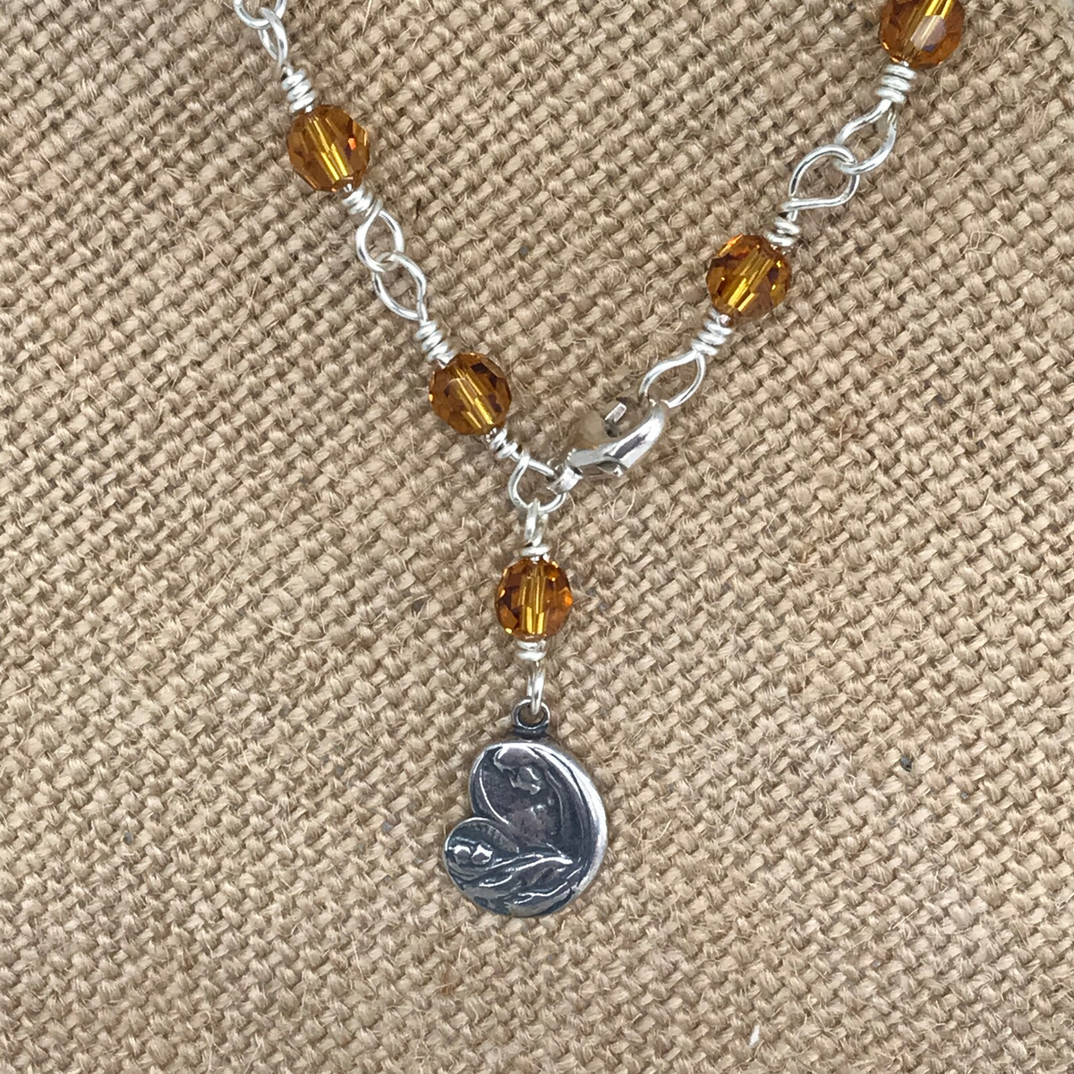 Golden amber crystal rosary bracelet detail with Madonna charm on burlap