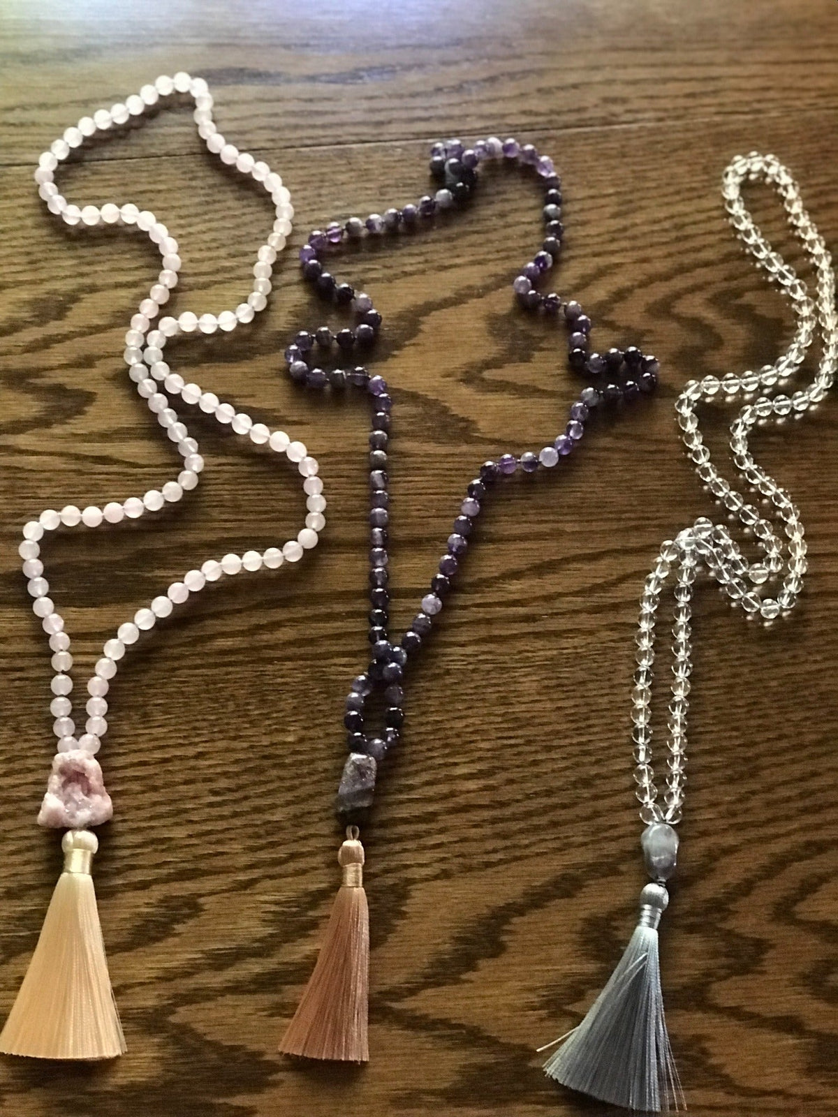 Three example malas with peach, copper and gray silk tassels on a wood table
