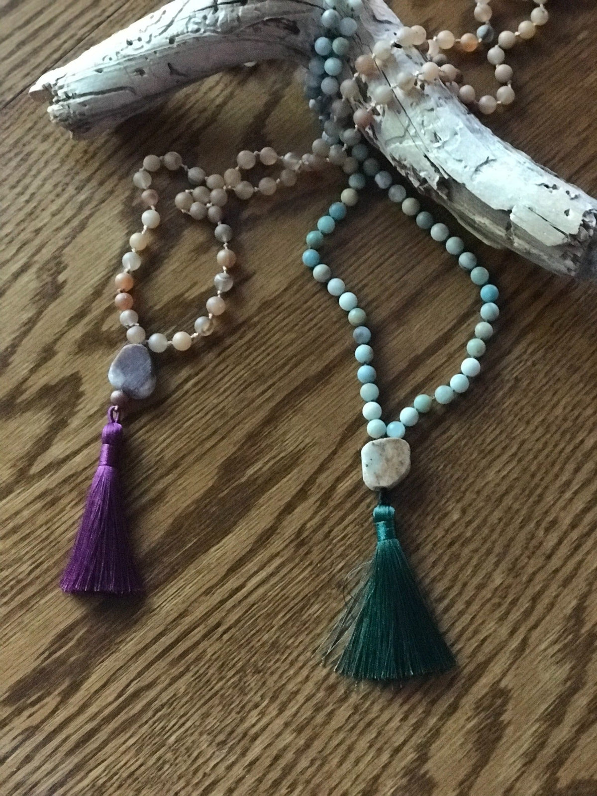 Example malas with purple and green silk tassels beside driftwood