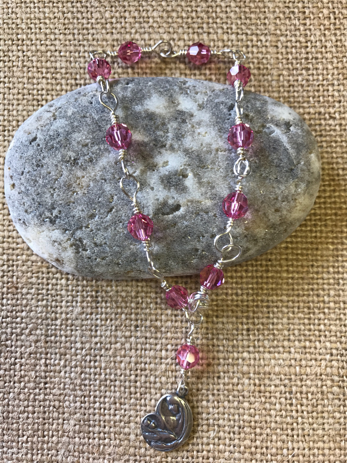 Rose pink crystal one-decade rosary bracelet with Madonna charm on gray stone and burlap